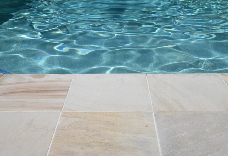 Carrelage extérieur en pierre claire antidérapante au bord d’une piscine.